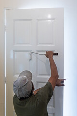 Person painting wooden white door with paint roller during home rennovation