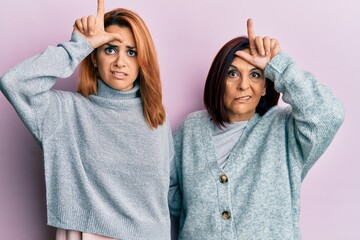 Latin mother and daughter wearing casual clothes making fun of people with fingers on forehead...