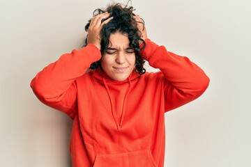 Young hispanic woman with curly hair wearing casual sweatshirt suffering from headache desperate and stressed because pain and migraine. hands on head.