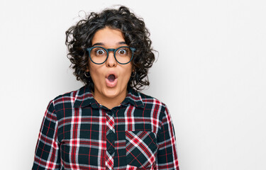 Young hispanic woman with curly hair wearing casual clothes and glasses scared and amazed with open mouth for surprise, disbelief face
