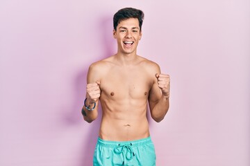Fototapeta premium Young hispanic man wearing swimwear shirtless celebrating surprised and amazed for success with arms raised and open eyes. winner concept.