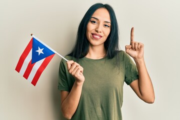 Young hispanic girl holding puerto rico flag smiling with an idea or question pointing finger with...