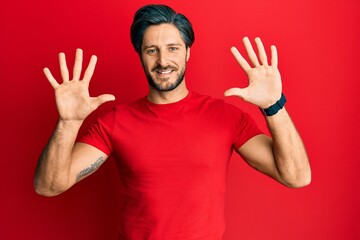 Naklejka premium Young hispanic man wearing casual red t shirt showing and pointing up with fingers number ten while smiling confident and happy.