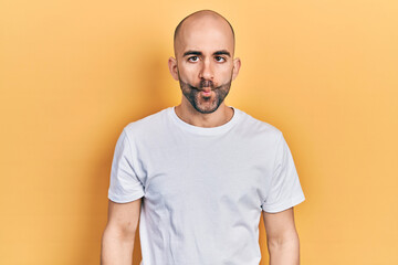 Young bald man wearing casual white t shirt making fish face with lips, crazy and comical gesture. funny expression.