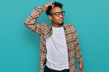 Young african american man with beard wearing casual clothes and glasses smiling confident touching hair with hand up gesture, posing attractive and fashionable