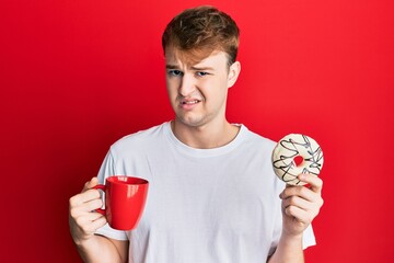 Young caucasian man drinking a cup of coffee and croissant clueless and confused expression. doubt...