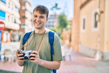 Young caucasian tourist man smiling happy using vintage camera at the city.