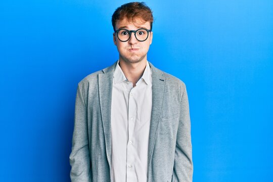 Young caucasian man wearing elegant clothes and glasses puffing cheeks with funny face. mouth inflated with air, crazy expression.