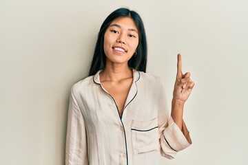 Young chinese woman wearing pajama pointing finger up with successful idea. exited and happy. number one.