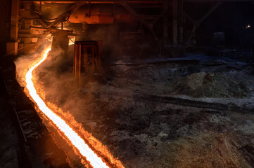 Fototapeta na wymiar The flow of molten hot metal, molten steel flows along the guide chute. Blast furnace