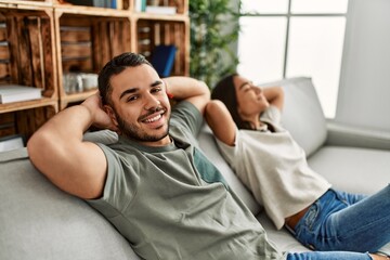 Young latin couple resting with head on hands sitting on the sofa at home.