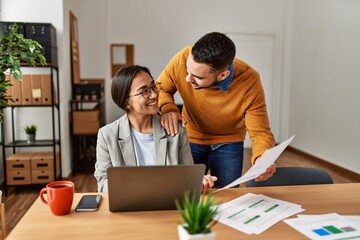 Two business workers smiling happy working sitting on desk at the office.