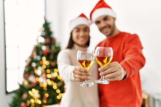 Young hispanic couple smiling happy toasting with champagne standing by christmas tree at home.