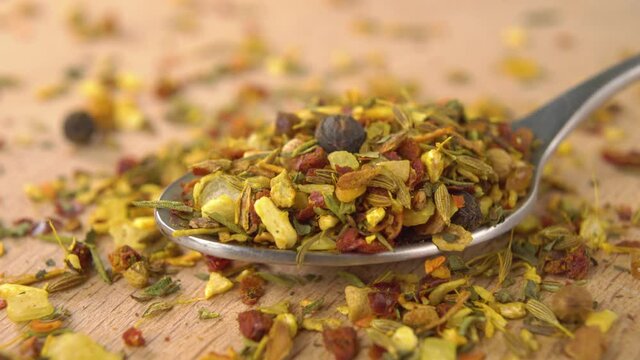 Full metal spoon spicy seasoning mix. Hot condiment with seeds and herbs on a wooden surface. Macro. Dolly shot.