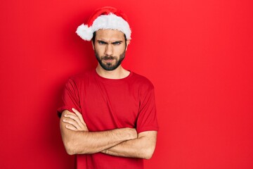 Fototapeta premium Young hispanic man wearing christmas hat skeptic and nervous, disapproving expression on face with crossed arms. negative person.