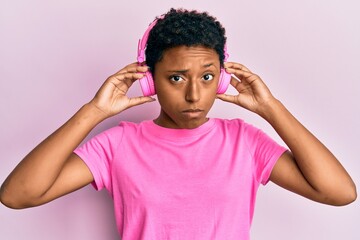 Young african american girl listening to music using headphones skeptic and nervous, frowning upset because of problem. negative person.