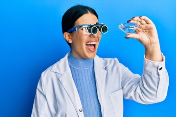 Beautiful brunette jeweller woman holding brilliant diamond stone wearing magnifier glasses smiling and laughing hard out loud because funny crazy joke.