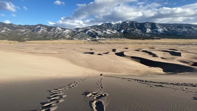 Great Sand Dunes, Colorado USA. Happy Man Running Down the Dune With Scenic Mountains in Background, Wide View