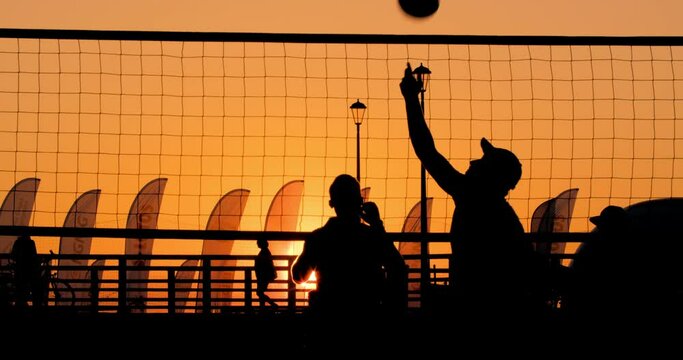 Silhouettes of people playing beach volleyball at sunset, a splash of volleyball in slow motion cinematic shooting. Silhouette of man hitting volleyball spike. 