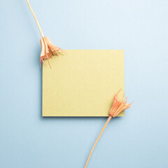 Yellow memo pad with pink dry flowers on blue background. top view, copy space