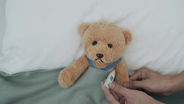 Using a bear as a child representation. man used a digital thermometer to measure his body temperature and found had a high fever put a cool gel pad over head to reduce the temperature.