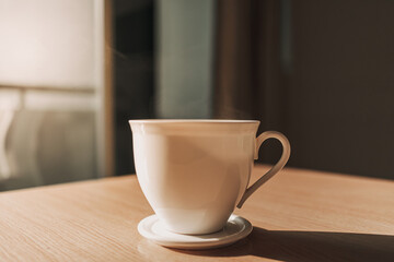 Obraz premium Hot cup of drink on the table in sun light of calm and warm morning.