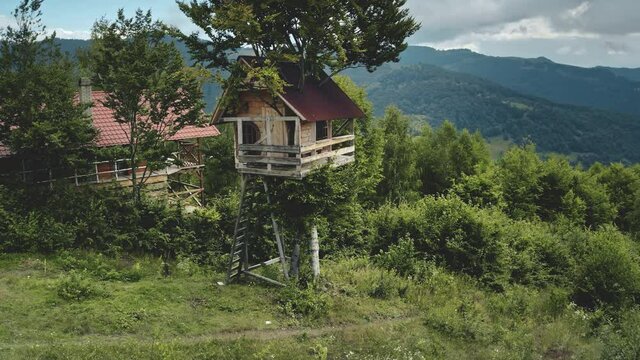 Aerial tree house on top forest slope, hotel in mountains. Wooden houses in countryside, eco tourism. Summer vacation in green Alps. Hiking, beautiful wilderness landscape natural light
