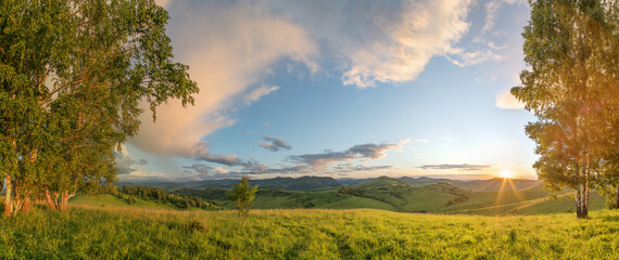 Summer evening, meadows, hills and forest. Sunset light and picturesque sky.