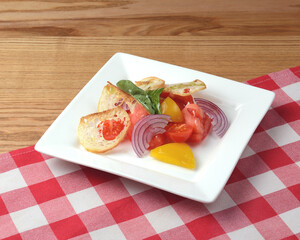Fresh tomatoes salad with onion and croutons served in a square plate over rustic wooden table with red plaid tablecloth
