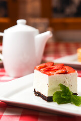 Strawberry cheesecake and fresh strawberries on top served on white plate on a rustic wooden table