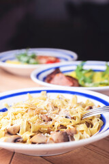Pasta Penne with chicken and mushroom under parmesan cheese served on a plate on a wooden table.