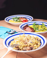Pasta Penne with chicken and mushroom under parmesan cheese served on a plate on a wooden table.