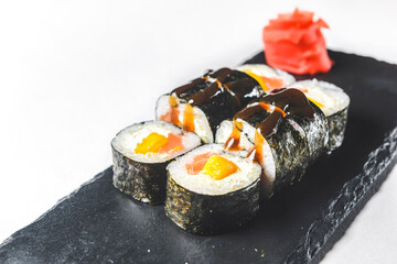 Fresh salmon sushi rolls with pickled ginger and wasabi on a black plate over white background.