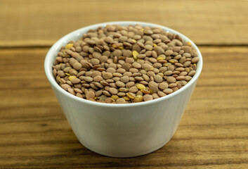 White ceramic bowl of green uncooked lentils isolated on wood in perspective.