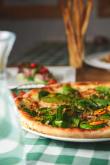 Delicious pizza with spinach and tuna shavings served on wooden table with green plaid tablecloth.