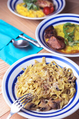 Pasta Penne with chicken and mushroom under parmesan cheese served on a plate on a wooden table.