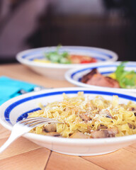 Pasta Penne with chicken and mushroom under parmesan cheese served on a plate on a wooden table.