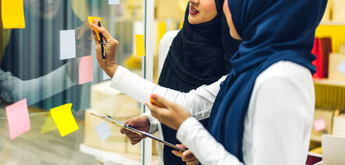 Two muslim business woman planning and brainstorm writing over the project with stickers note on glass window at modern office.Teamwork concept
