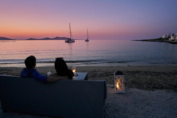 Idyllic view of a couple sitting on a sofa gazing the sunset by the sea in the picturesque seaside...