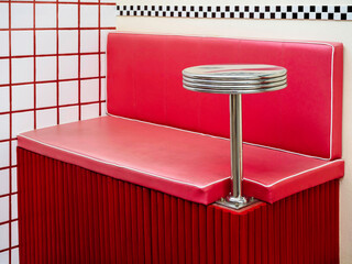 Empty round stainless steel side table fixing on red retro style diner booths. Mini round drink stand on empty red leather vintage bar bench seat near white tiles wall background.