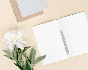 Top view of open notebook with blank pages and white peony flower on table. Creative workspace