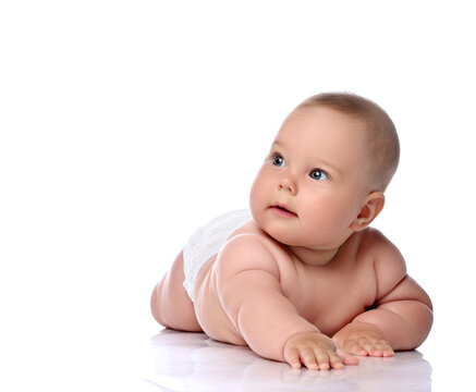 Surprised infant child baby girl kid in diaper is lying on her stomach, slapping on floor and looking at copy space at upper corner isolated on a white background