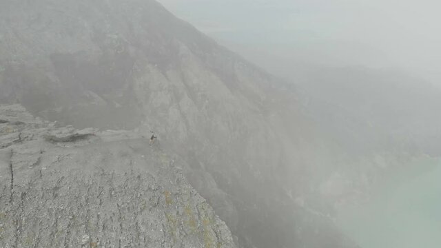 Person standing on edge of Ijen volcano taking photos with mist, aerial