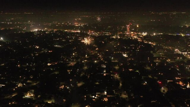 An aerial view of Fourth of July fireworks set off by the locals on Long Island, NY. The drone camera dolly in, high over the suburban neighborhood as red fireworks go off below.
