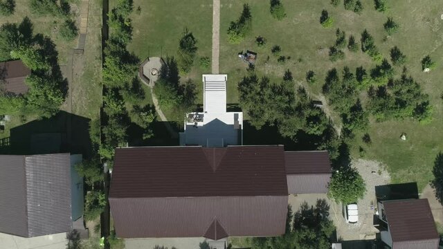 Aerial view of The backyard of the banquet house for celebrations and weddings. In the courtyard there is a white porch, a lawn, a path made of stones, trees and a barbecue area. A man and a woman are