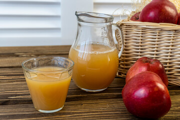 Red apples in a basket and apple juice in a jug on a wooden table