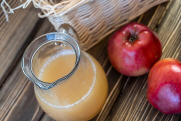 Red apples in a basket and apple juice in a jug on a wooden table