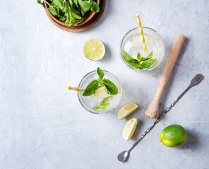 Concept flatlay mojito drink. Two glasses of lime lemonade with lime slices,  juicer, spoon and...