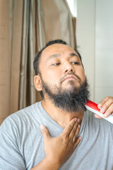 Obraz premium Asian man shaving beard with electric razor machine.