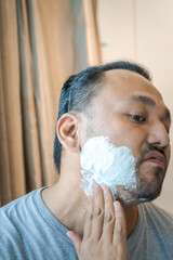 Applying shaving cream on the face of an Asian man.